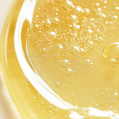 Close-up of golden gel cleanser in petri dish with fine bubbles showing the lightweight texture of Symbiome The Renewal Daily Cleanser