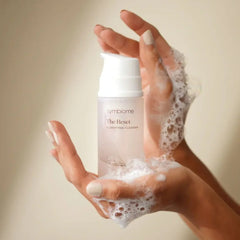 Hands holding Symbiome The Reset Clarifying Cleanser bottle with foamy lather
