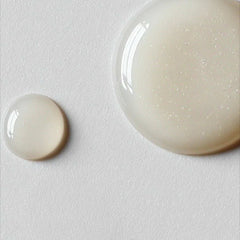 Two pearlescent serum droplets on white surface showing the lightweight gel texture of Symbiome The Solution neck serum