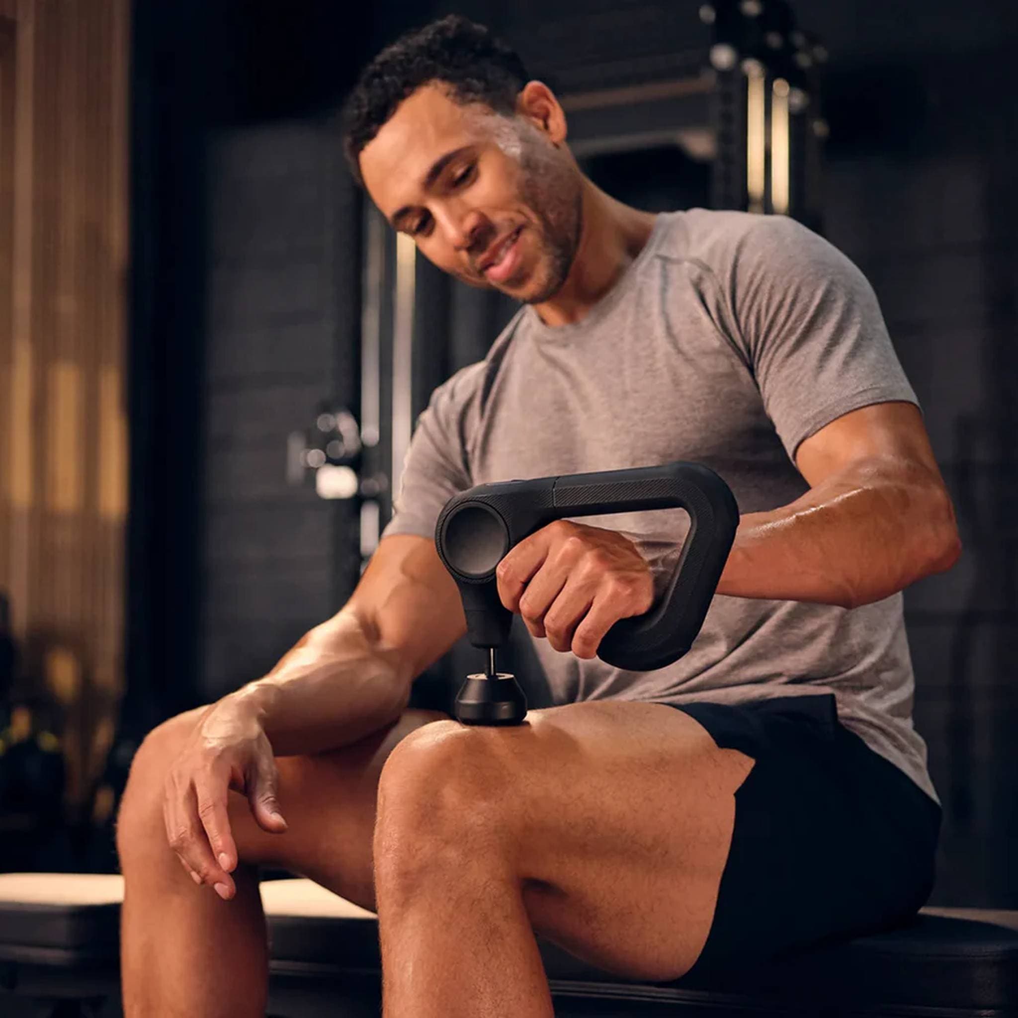 Close-up of a man using Theragun Prime massage gun on his thigh in the gym