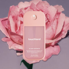Touchland Glow Essence Blush Rose fragrance mist in front of a large pink rose on a lilac background