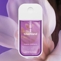 Touchland Power Essence Cashmere Woods fragrance mist in front of a soft white orchid on purple