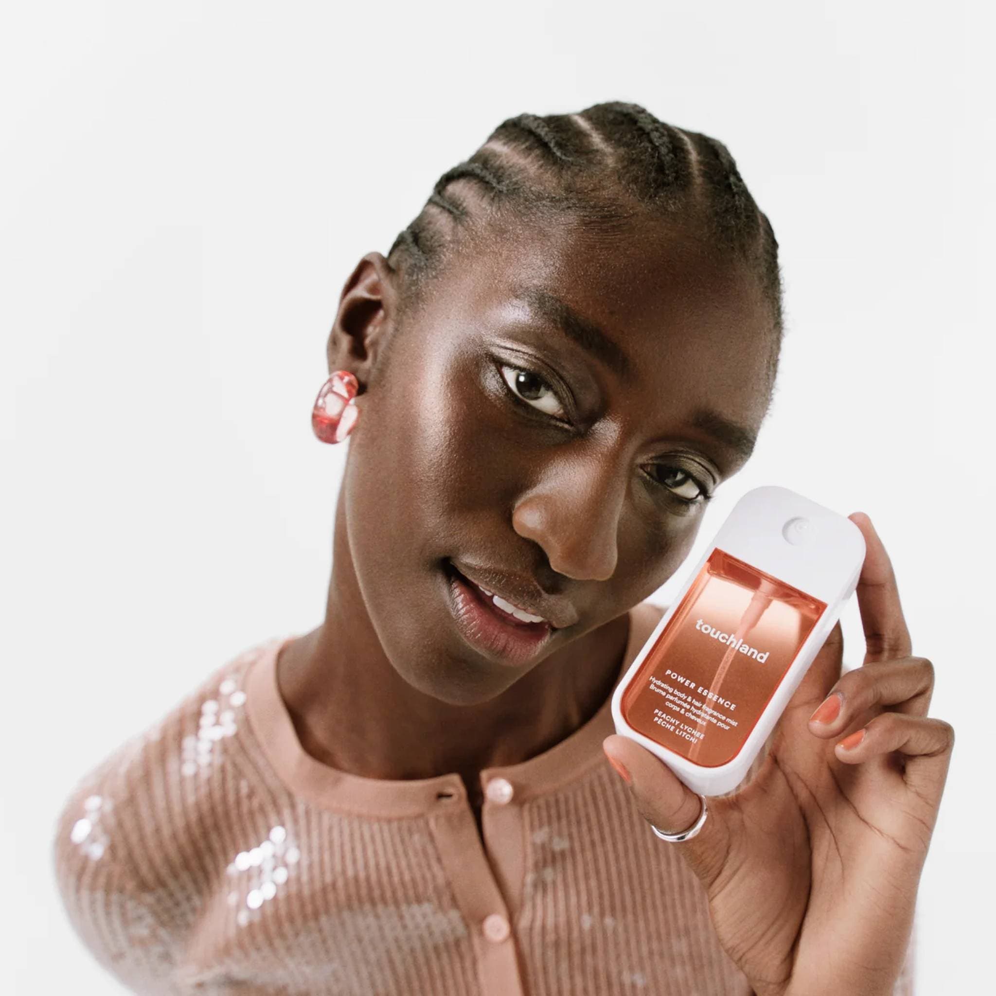 Woman with braided hair in a blush sequin cardigan holding Peachy Lychee Power Essence fragrance mist to her face