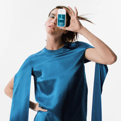 Woman in a teal satin top holding Sparkling Bergamot Power Essence fragrance mist over one eye