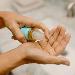 Person applying a clear liquid from a bottle with a blue label onto their palm.